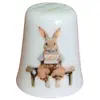 Foto de um(a) Dedal de Coleção em Porcelana - Estampa Casal de Coelhos e Coelhinho no Banco, da categoria de Outros colecionáveis. Este é um delicado dedal colecionável em porcelana branca, que apresenta uma temática lúdica e clássica de "Easter Bunnies"... Vendido no marketplace Trésors.