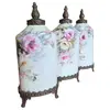 Foto de um(a) Trio de Potes em Porcelana Pintada à Mão com Base e Tampa em Bronze - Estilo Floral Clássico, da categoria de Garrafas, potes e jarros. Apresentamos este magnífico trio de potiches (vasos com tampa) em porcelana de alta qualidade, apresentando um formato... Vendido no marketplace Trésors.