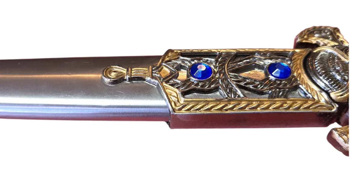 Foto de um(a) Adaga Decorativa de Fantasia com Bainha – Detalhes em Relevo e Cristais Sintéticos Azuis, da categoria de Facas. Adaga decorativa com design inspirado na fantasia épica, apresentando um acabamento refinado em tons de prata e ouro... Mostrado de uma perspectiva diferente. Vendido no marketplace Trésors.