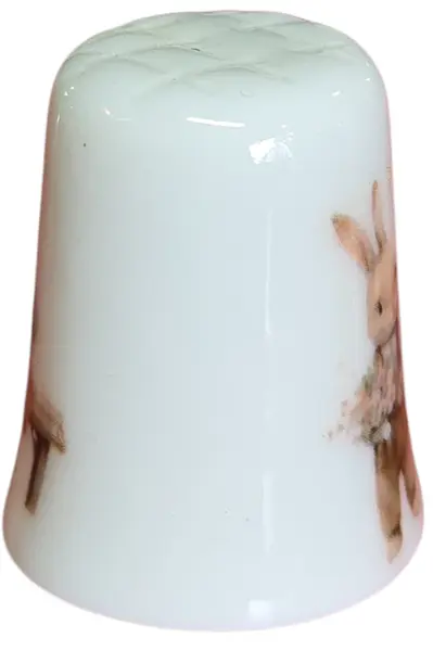 Foto de um(a) Dedal de Coleção em Porcelana - Estampa Casal de Coelhos e Coelhinho no Banco, da categoria de Outros colecionáveis. Este é um delicado dedal colecionável em porcelana branca, que apresenta uma temática lúdica e clássica de "Easter Bunnies"... Mostrado de uma perspectiva diferente. Vendido no marketplace Trésors.